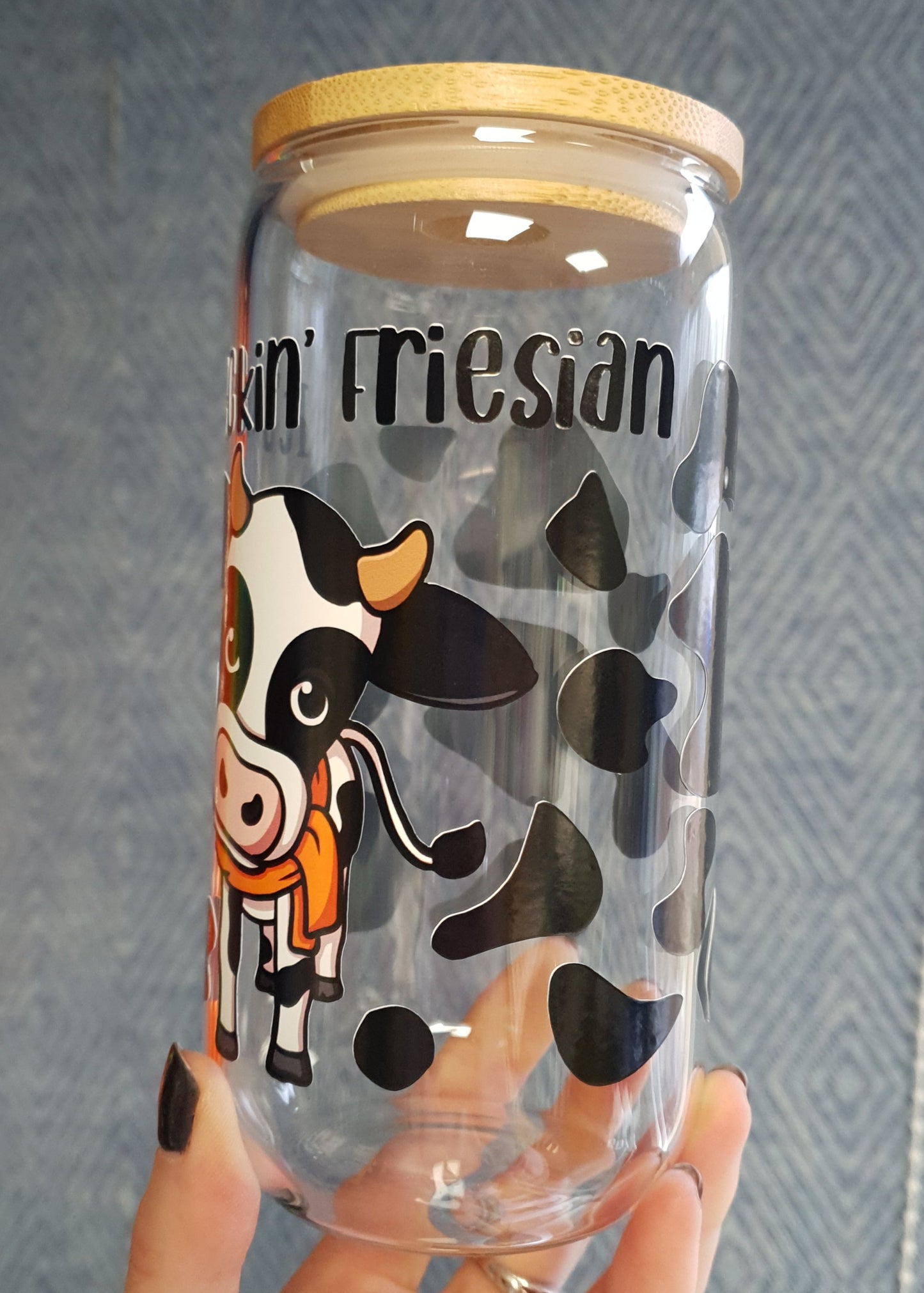 Clear tumbler with cartoon cow design and 'It's Feckin Friesian' text, held by a hand on a textured surface.