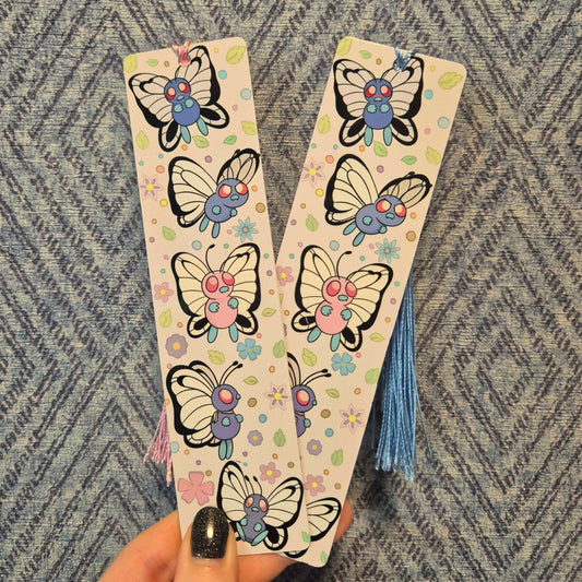 Two decorative bookmarks with butterfly designs held against a textured fabric background.