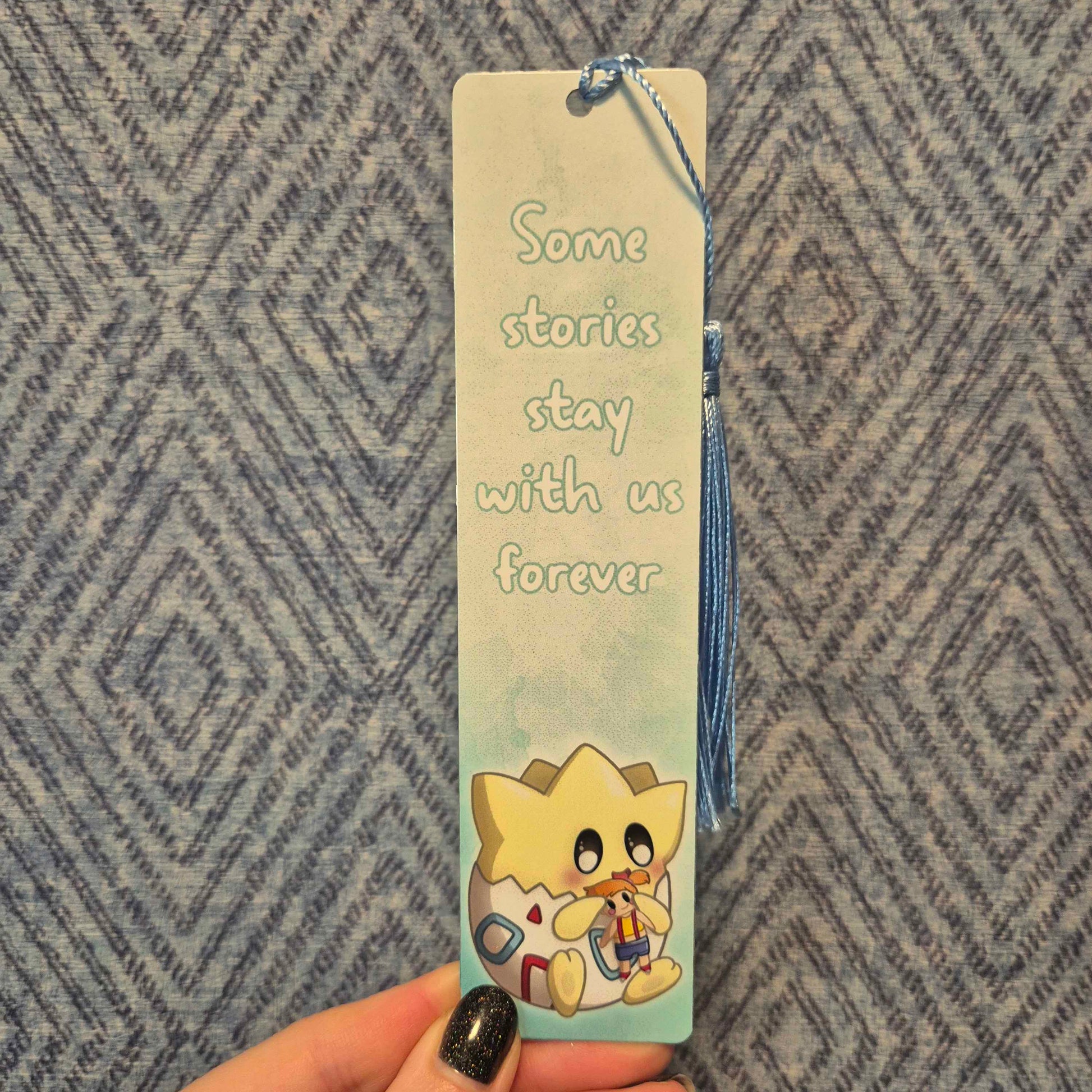 Bookmark with cartoon character and text held by a hand against a patterned background