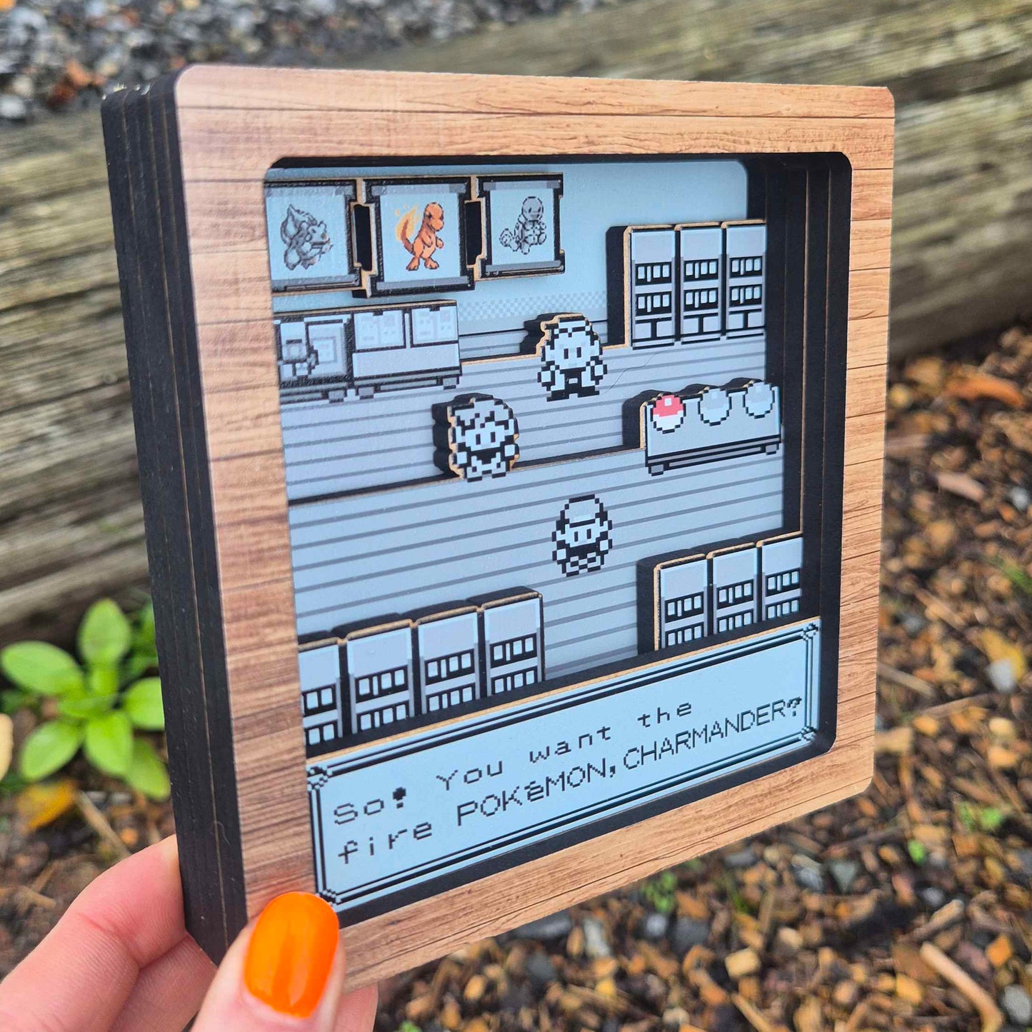 Small framed artwork resembling a classic video game interface held by a hand outdoors.