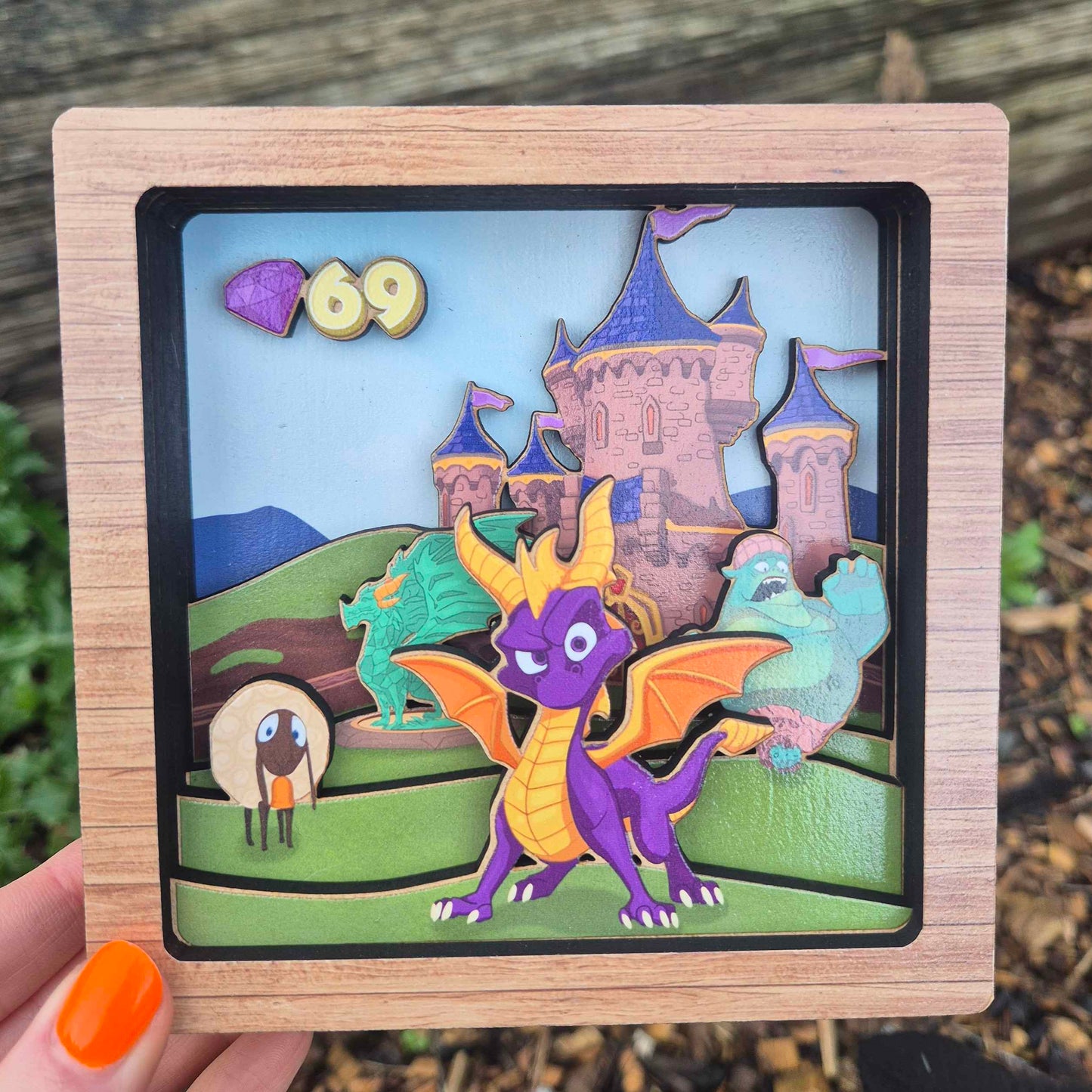 Wooden frame with a colorful cut-out design of a dragon and castle, held outdoors.