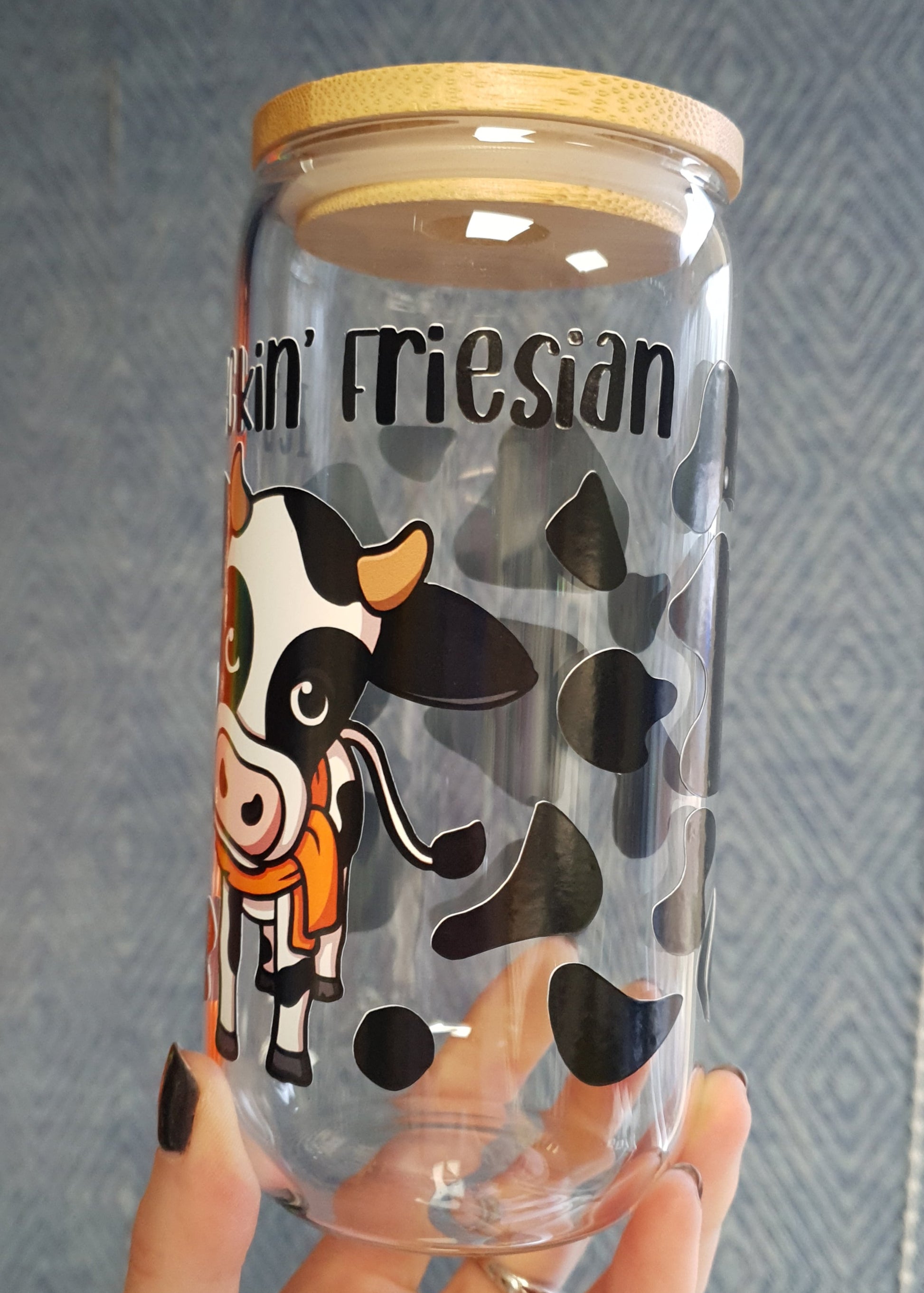 Clear tumbler with cartoon cow design and 'It's Feckin Friesian' text, held by a hand on a textured surface.