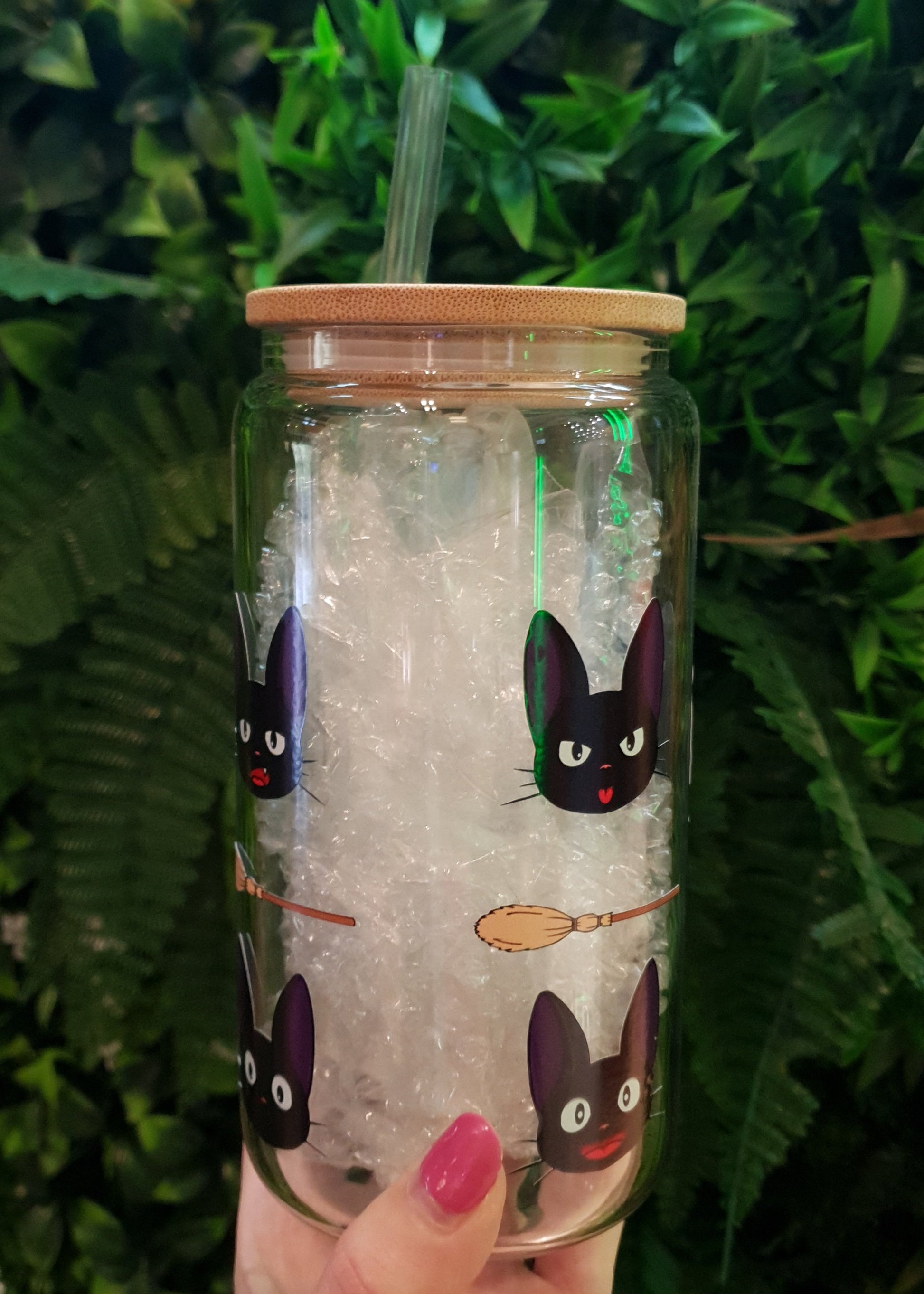 Clear tumbler with cartoon cat design held against a green leafy background