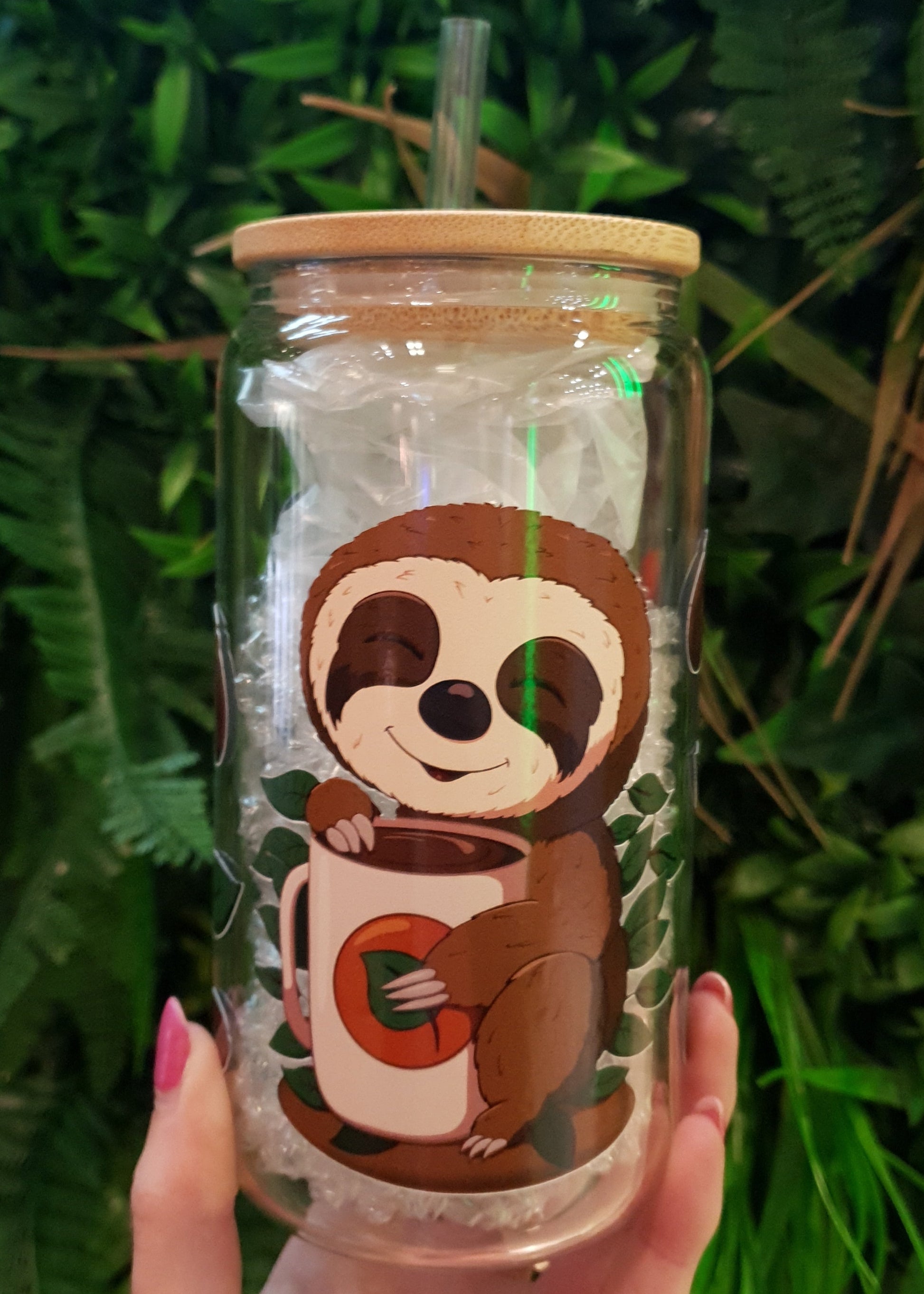 Clear tumbler with sloth design held in front of green foliage