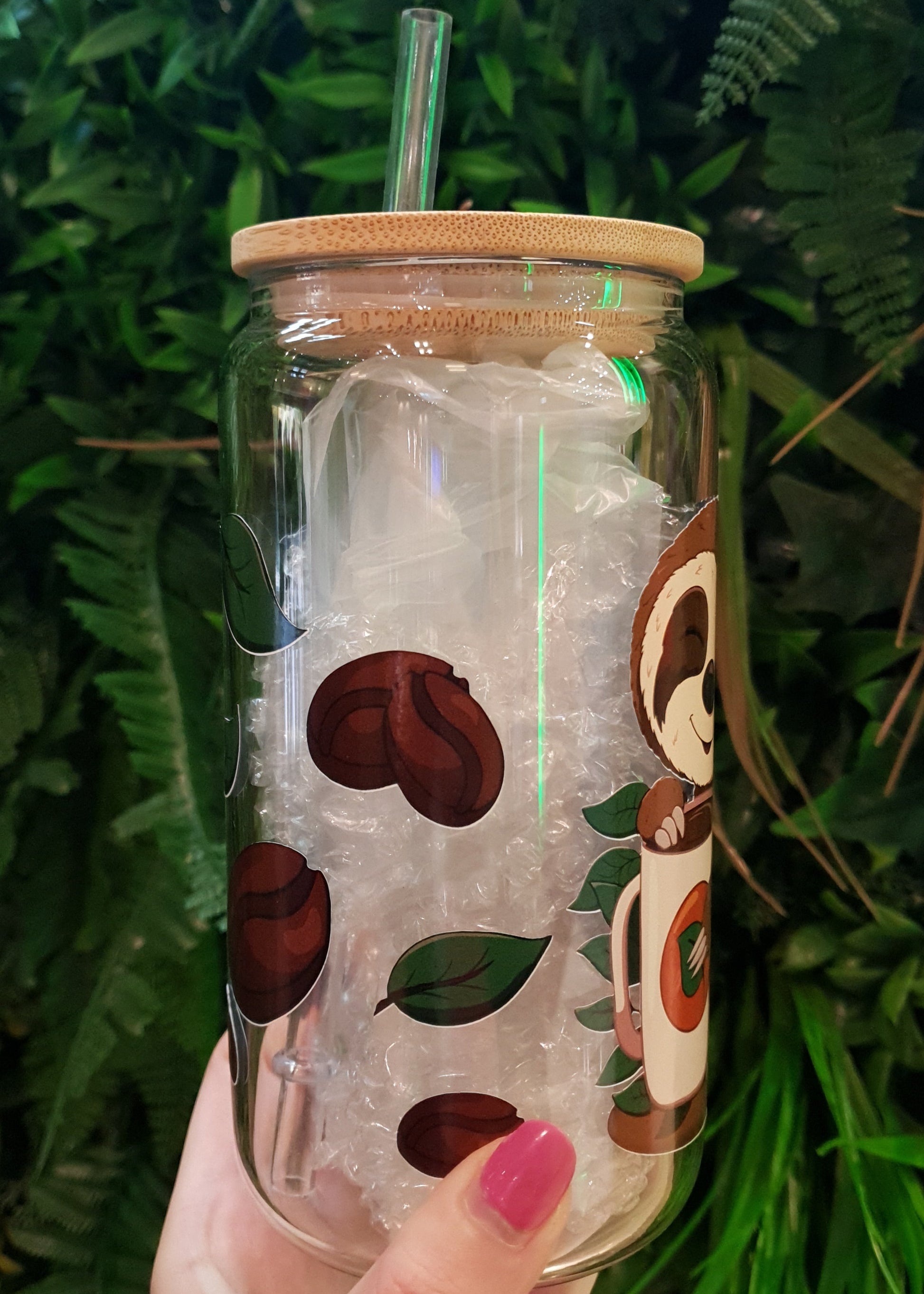Clear tumbler with coffee bean design held by a hand against a green leafy background